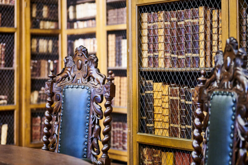 Two wooden chairs in front of bookcases with old books